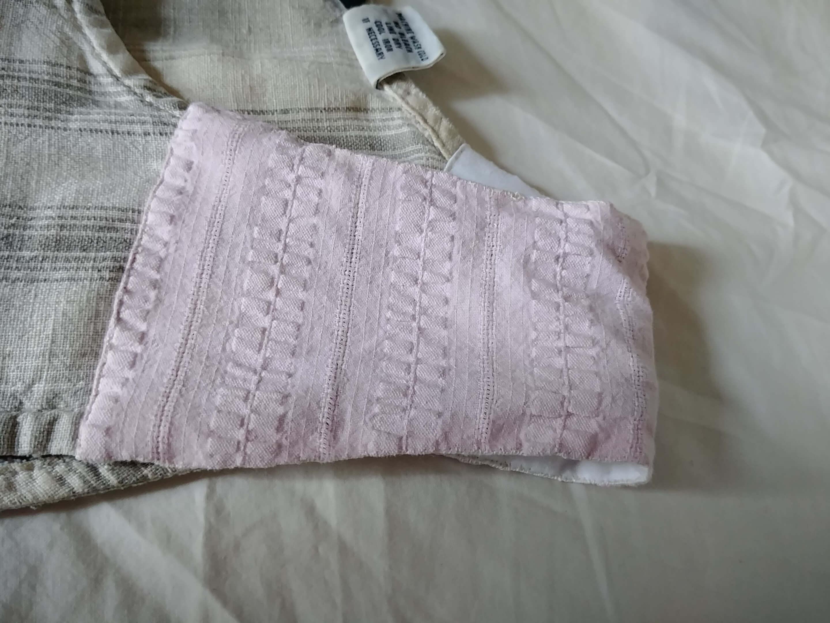 The shoulder of a white sleeveless dress with grey stripes has a large patch of pink fabric with a texture of raised, bumpy stripes
