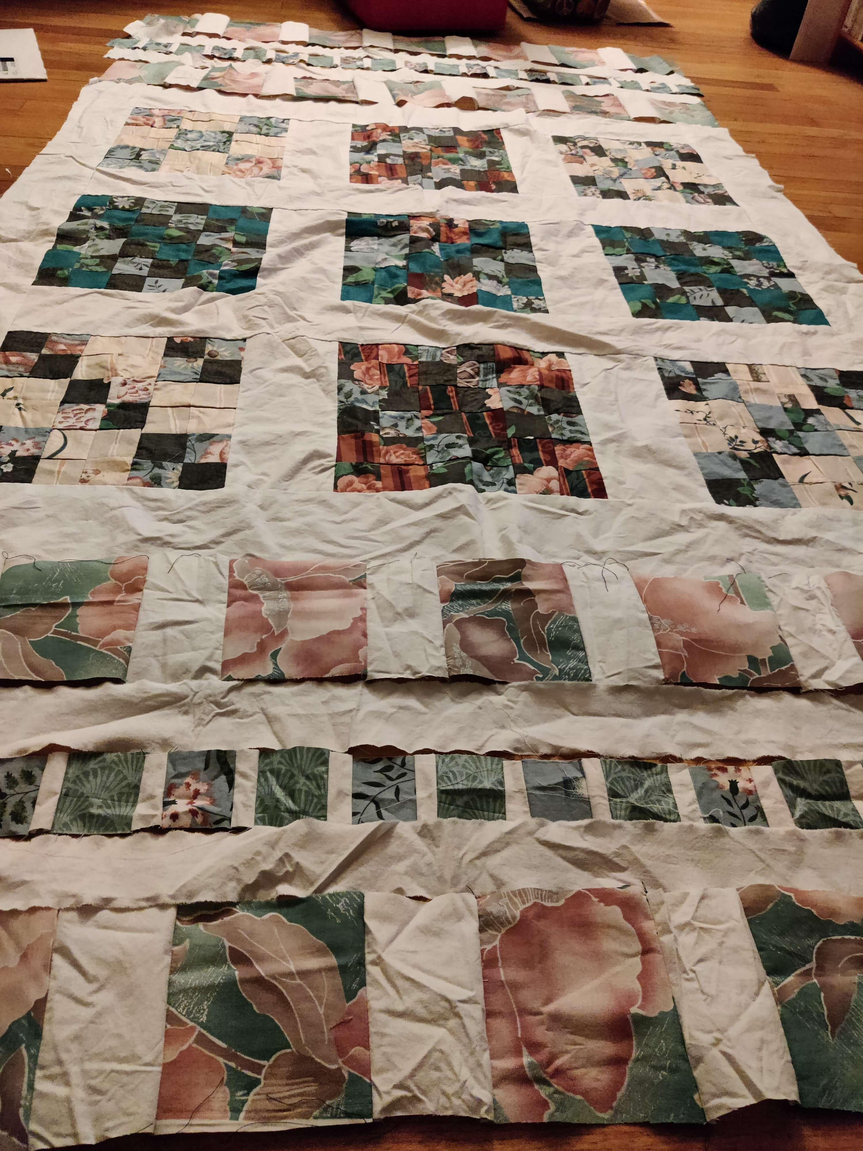 a very wrinkly patchwork quilt top in progress, with various sized squares of pink and blue floral fabric bordered with white