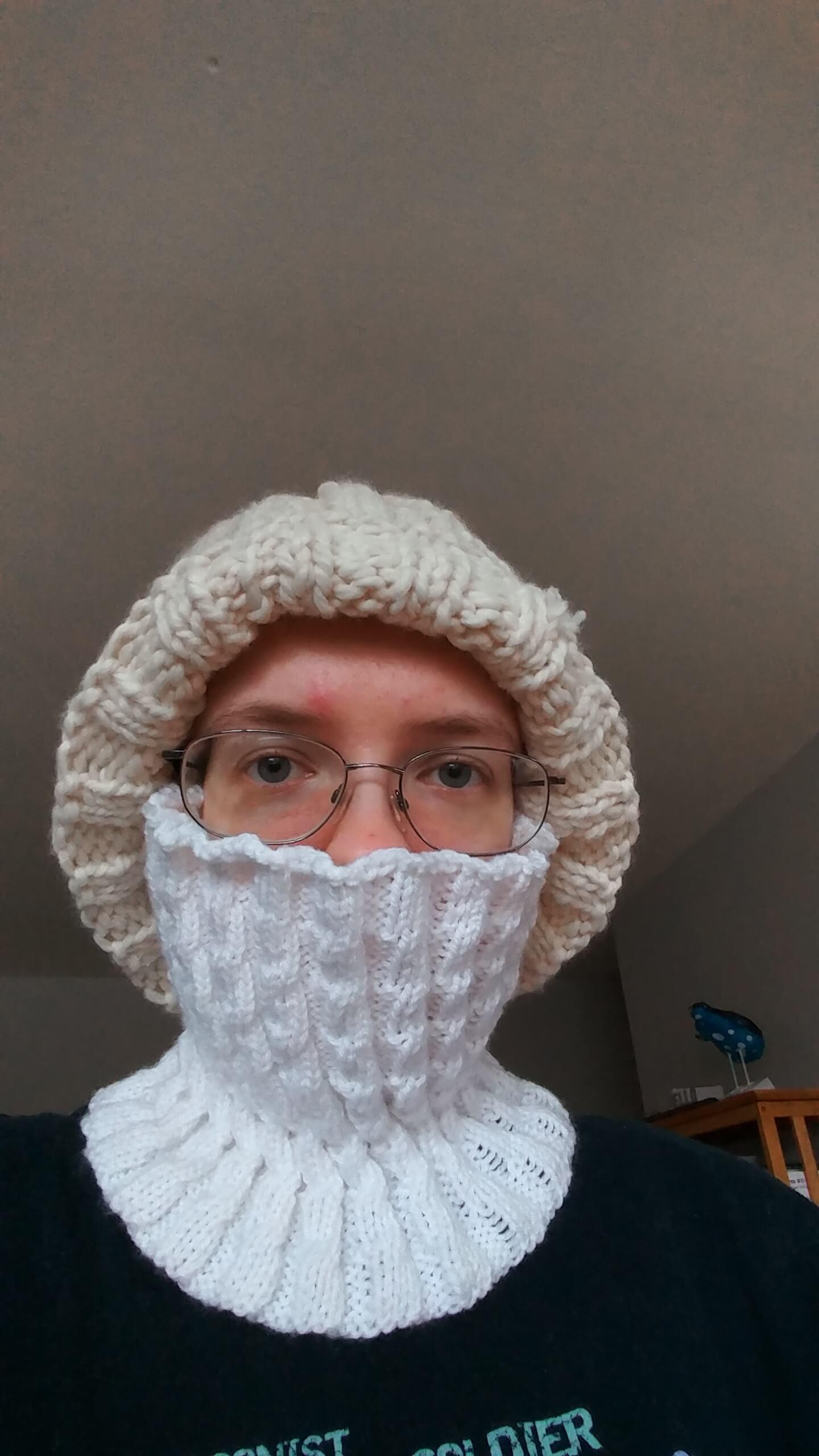 Me wearing the helical cowl, which has a spirally ribbed pattern, pulled up to my nose, with a white knit hat on top