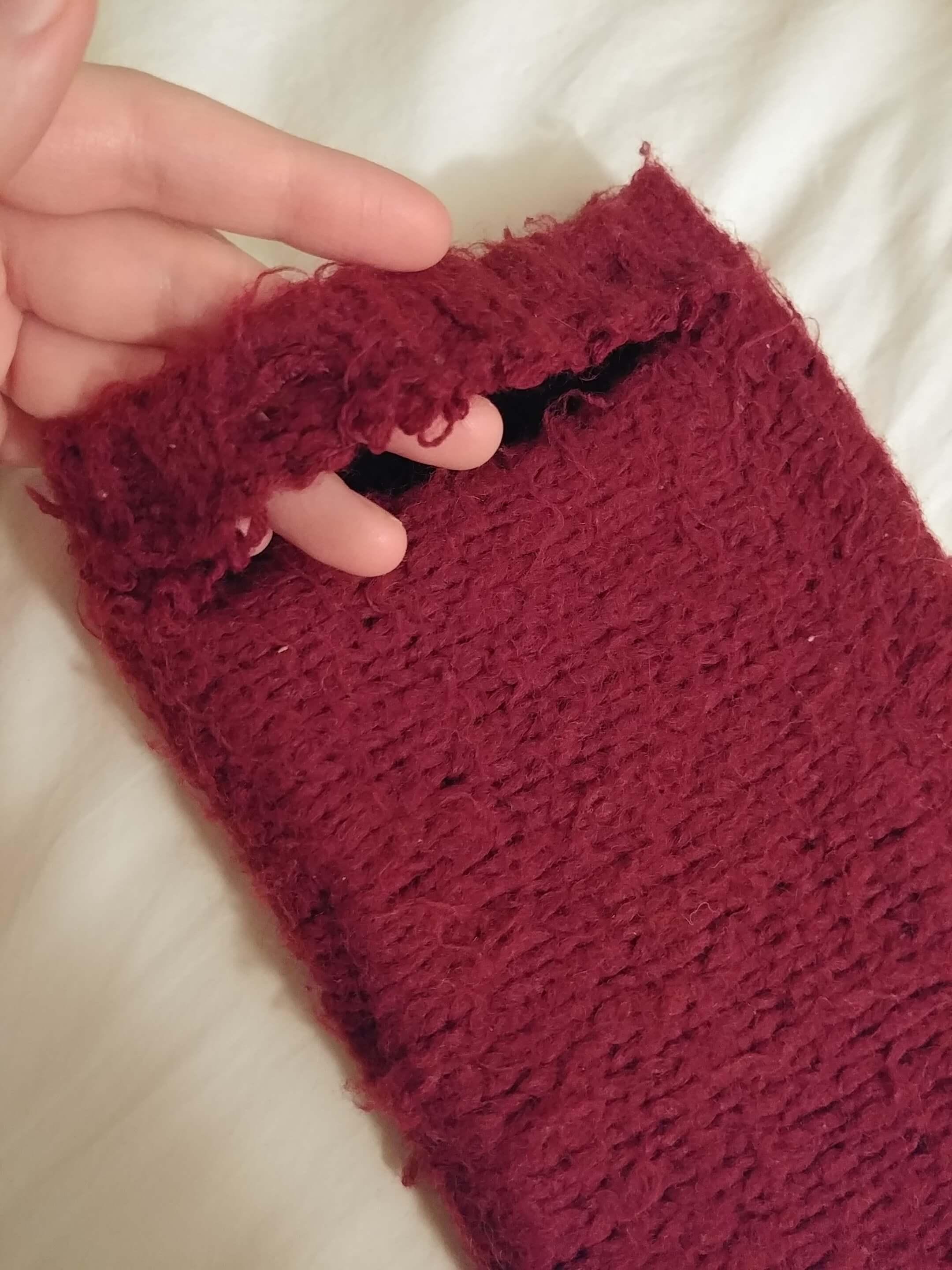 Sticking my fingers through a large horizontal rip in a maroon fabric Kindle case 