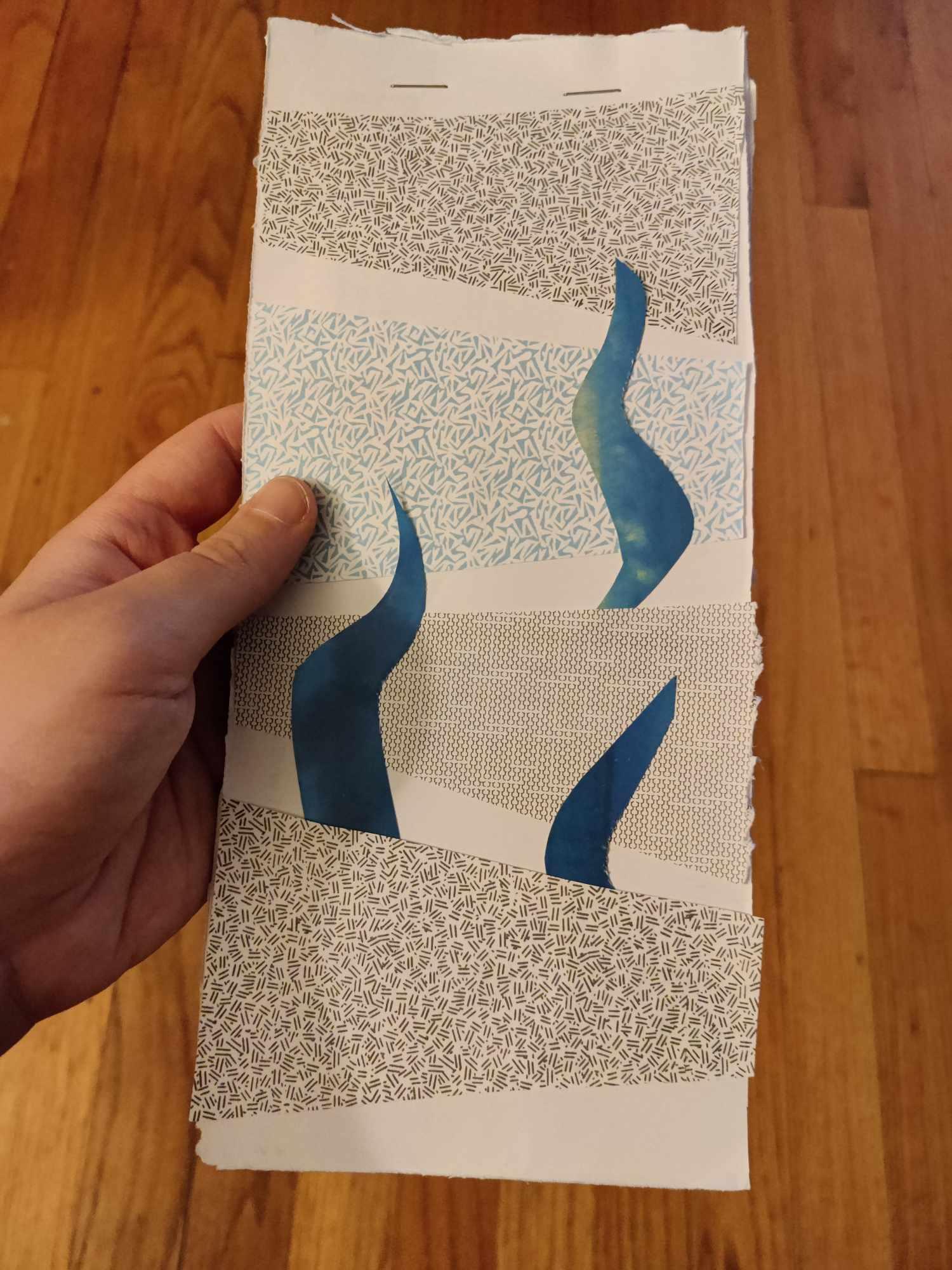 a makeshift notebook made of cut-up envelopes stapled together at the top, with an abstract collage of blue and grey patterned paper on the front