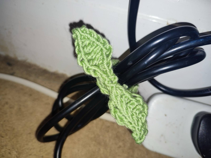 A twin leaf shaped tie around a bundle of black cables. The cotton yarn is light green.