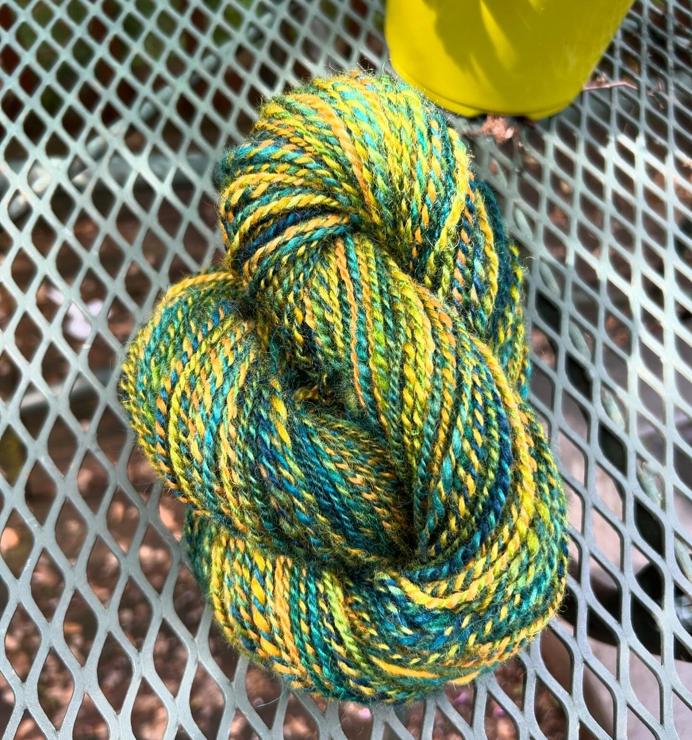 A twisted skein of handspun wool yarn in spirals of greens, yellows, and blues.  It's photographed outside on a sunny day and it looks joyful and squishy. 