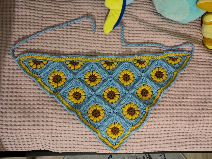 Blue crochet bandana with a sunflower pattern on it and yellow stripe around the edges