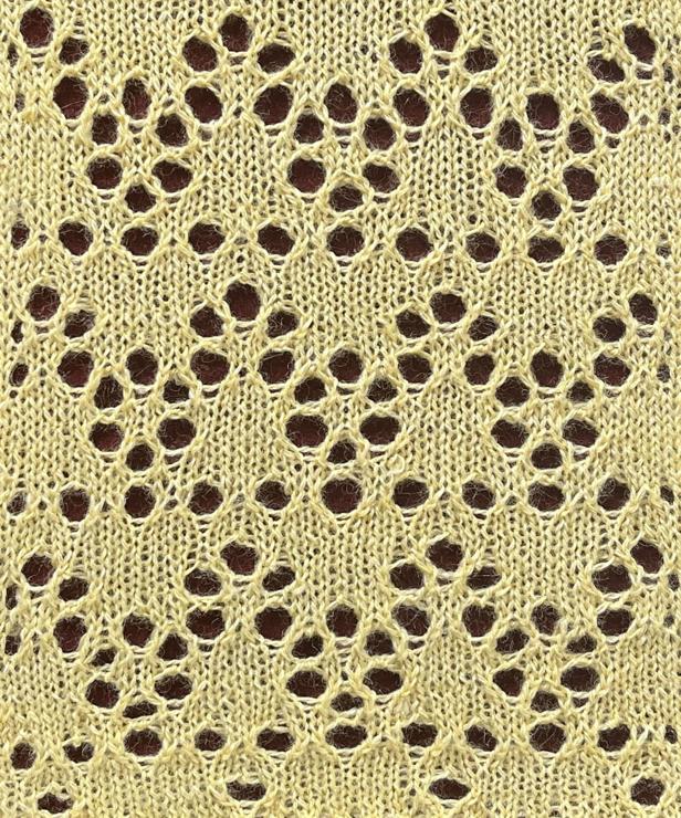 Knitted sample of Cedar lace in yellow yarn making  a complex lacy zigzag with six-petaled flower shapes and arches joining them, alternating with horizontal dashed lines.