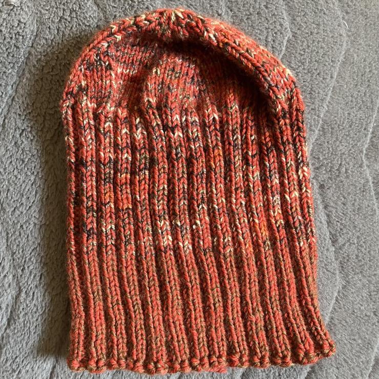 A hand knitted beanie with a smooth top and ribbed sides for stretchiness. 

Most of the hat is knit with a rusty orange yarn held together with a grey, black, cream, and orange yarn. The bottom edge is rusty orange held together with medium brown. 